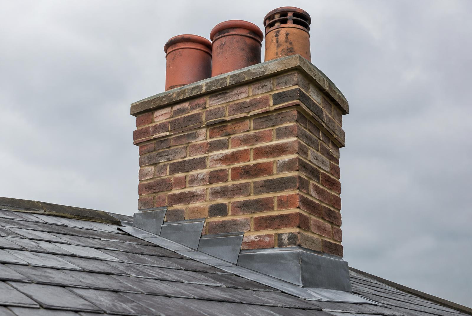 Brick chimney stack with clay pots and new lead flashing on a slate roof